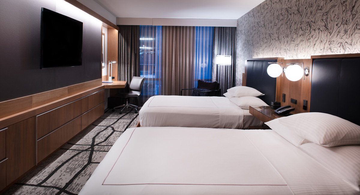 A hotel room with two twin beds, a desk, TV, and window